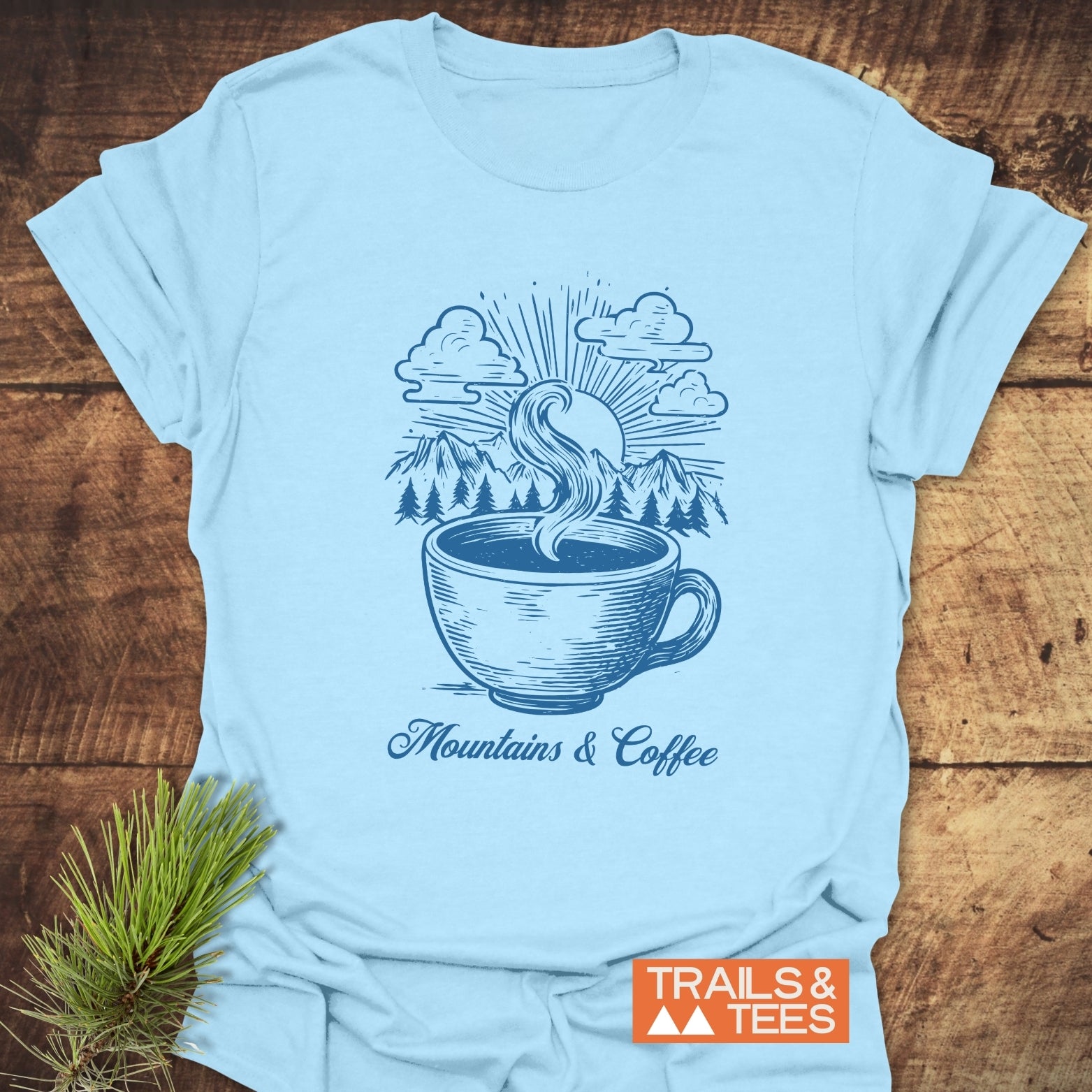 Mountains And Coffee T-Shirt featuring a stylized coffee cup design with mountains and sunburst, promoting outdoor adventure and comfort.