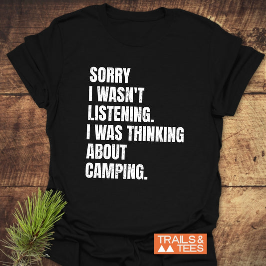 Black T-shirt with SORRY I WASN'T LISTENING. I WAS THINKING ABOUT CAMPING. in white. Orange TRAILS & TEES. logo. Pine sprig beside.