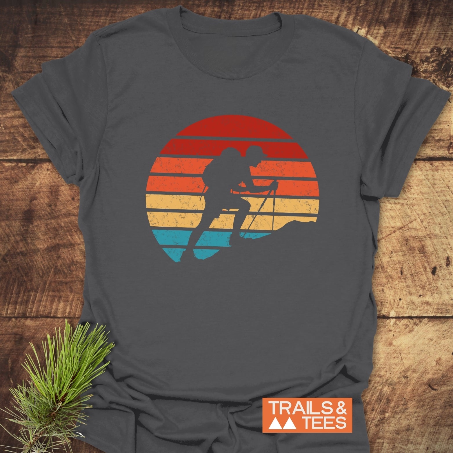 Uphill Hiker T-Shirt with vintage sunset graphic and backpacker silhouette, laid on rustic wood. Features soft ring-spun cotton, durable print, pre-shrunk for reliable fit.