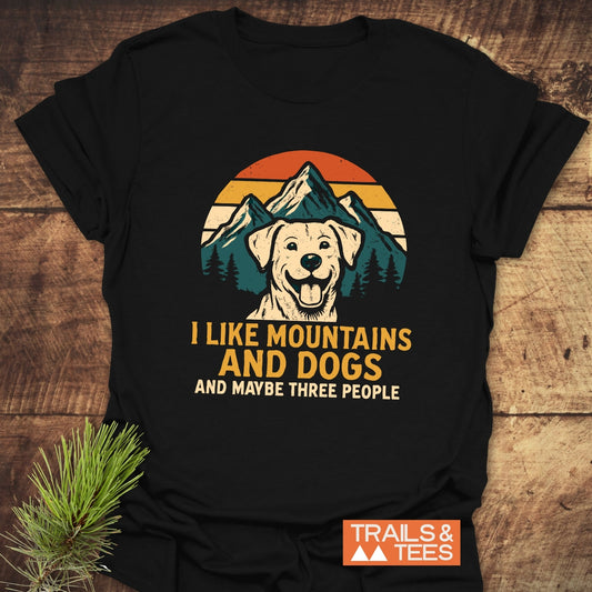 Black T-shirt featuring a cartoon dog, mountains, and sunset graphic with the text I LIKE MOUNTAINS AND DOGS, emphasizing outdoor adventure and comfort.