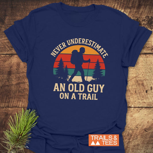 Never Underestimate T-Shirt features a hiker silhouette with a sunset backdrop on navy fabric, highlighting trail-tested comfort and durable prints.