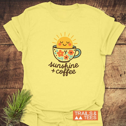 Sunshine And Coffee T-Shirt featuring a smiling sun in a floral mug graphic, hand-lettered phrase, on soft, lightweight cotton, beside a pine sprig.
