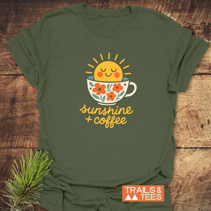 Sunshine And Coffee T-Shirt featuring a sun in a coffee cup with floral accents, laid flat on wood, embodying outdoor adventure and comfort by TRAILS & TEES.