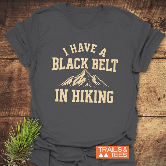 Black Belt In Hiking T-Shirt with mountain graphic and slogan. Soft ring-spun cotton, pre-shrunk, durable print. Designed for outdoor enthusiasts.
