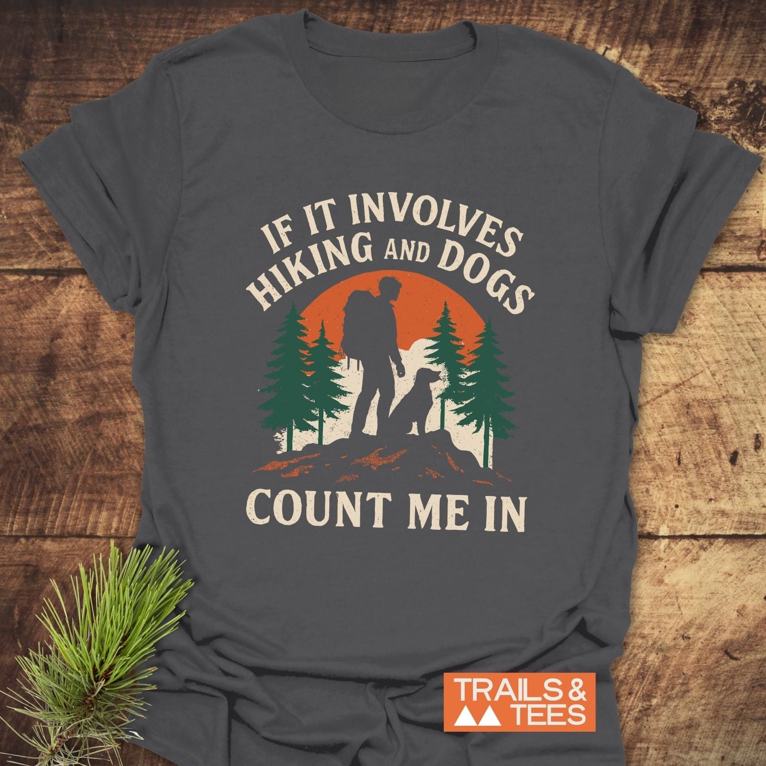 Hiking And Dogs T-Shirt: Dark-gray with a backpacker and dog silhouette against an orange sun, surrounded by pine trees. IF IT INVOLVES HIKING AND DOGS, COUNT ME IN.