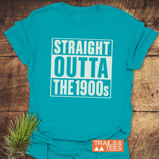 Teal t-shirt with STRAIGHT OUTTA THE 1900s in white block letters, showcasing Trails & Tees logo, alongside pine needles.