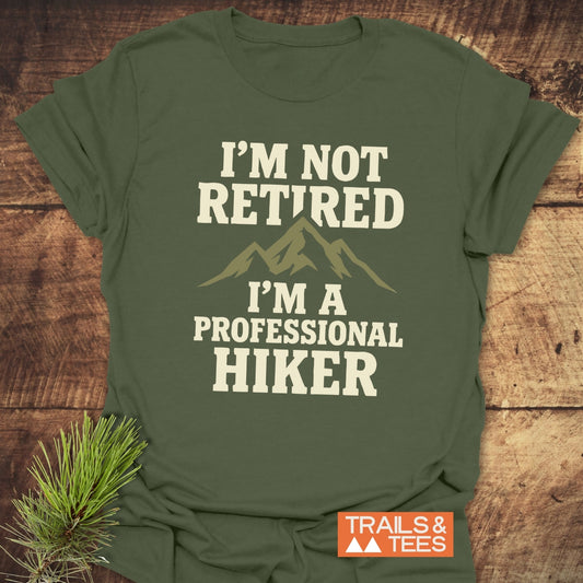 Forest-green I'm Not Retired t-shirt with mountain graphic, styled with pine sprig, showcasing soft cotton and durable print for outdoor enthusiasts.