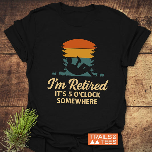I'm Retired, 5 O'Clock T-Shirt with sunset, hammock graphic, and Trails & Tees logo on rustic wood, evoking laid-back, outdoorsy vibes.