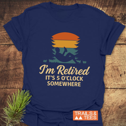 Navy-blue T-shirt featuring a sunset and reader graphic with “I’m Retired – It’s 5 O’Clock Somewhere,” highlighting comfort and durability.