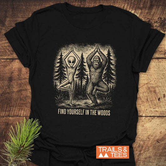 Find Yourself In The Woods T-Shirt featuring an alien and Bigfoot in yoga pose, with slogan. Made from soft cotton, ideal for outdoor enthusiasts.
