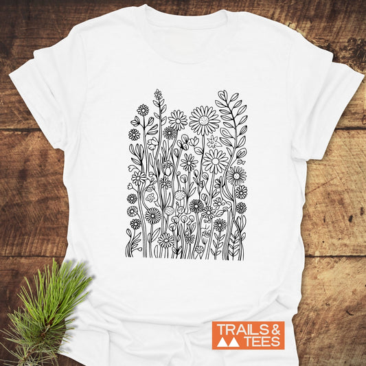 Wildflowers T-Shirt featuring black line-art of daisies and buds on white cotton, with an orange TRAILS & TEES logo, perfect for outdoor enthusiasts.