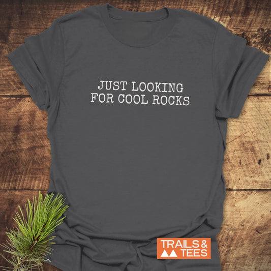 Dark-gray crewneck T-shirt with “JUST LOOKING FOR COOL ROCKS” in white letters, beside pine needles. Features soft ring-spun cotton, pre-shrunk fit, durable print.