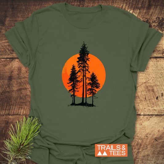 Sunset Trees T-Shirt with black pine silhouettes on an orange sun. Olive-green, crafted from soft cotton, perfect for outdoor enthusiasts. Includes TRAILS & TEES logo.