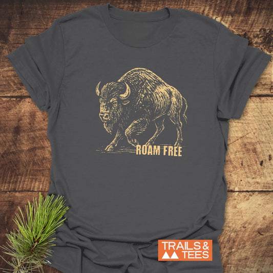 Roaming Bison T-Shirt: Charcoal-gray tee with tan bison illustration and ROAM FREE slogan, brand label visible, pine sprig accentuates wilderness theme.