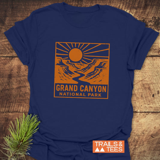 Grand Canyon NP T-Shirt displaying a canyon scene graphic and text, laid on wood with pine sprig, embodies outdoor adventure and comfort with durable, lightweight cotton.
