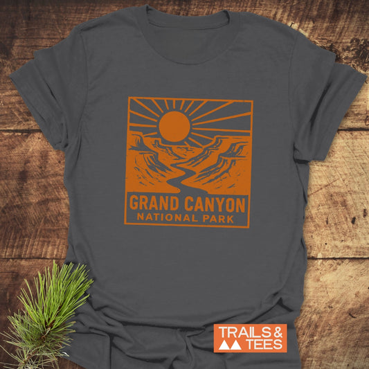 Charcoal-gray Grand Canyon NP T-Shirt with a burnt-orange canyon print, highlighting trail-ready comfort and durability, laid on a wooden surface with pine sprig.