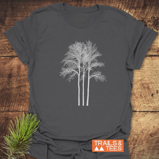 Tree Silhouettes T-Shirt with minimalist tree graphic on charcoal-gray fabric, laid on wood. Features pre-shrunk, lightweight cotton for comfort, ideal for outdoor enthusiasts.