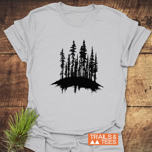 Woods Silhouette T-Shirt featuring a black evergreen tree cluster design on light gray fabric, displayed with a pine sprig, emphasizes outdoor adventure and comfort.