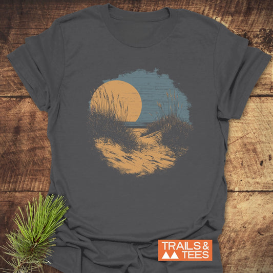 Indiana Dunes National Park T-Shirt on rustic wood, featuring a scenic dune path graphic under an orange sun. Includes a TRAILS & TEES logo and pine needle accent.