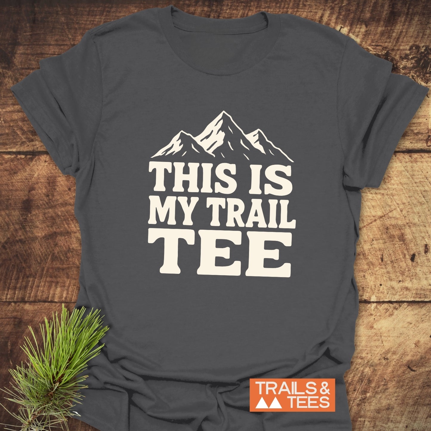 Charcoal-gray T-shirt with “THIS IS MY TRAIL TEE” text and mountain graphic, by TRAILS & TEES. Made from soft cotton, ideal for outdoor adventures.
