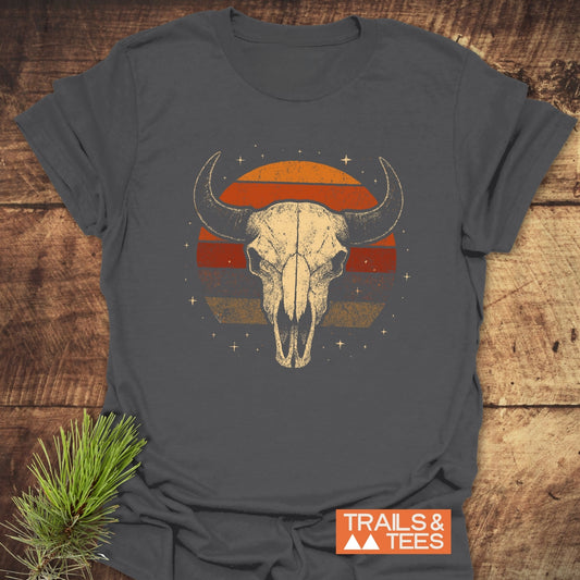 Retro Buffalo Skull T-Shirt on rustic wood, featuring a stylized skull over a sunset circle. Soft, pre-shrunk cotton with durable print, perfect for outdoor adventures.