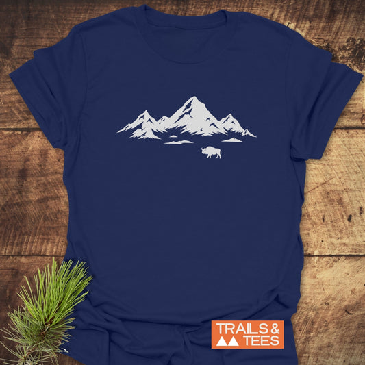 Mountains And Buffalo T-Shirt features a stylized mountain range and bison silhouette, displayed on a navy-blue tee with an orange TRAILS & TEES label.