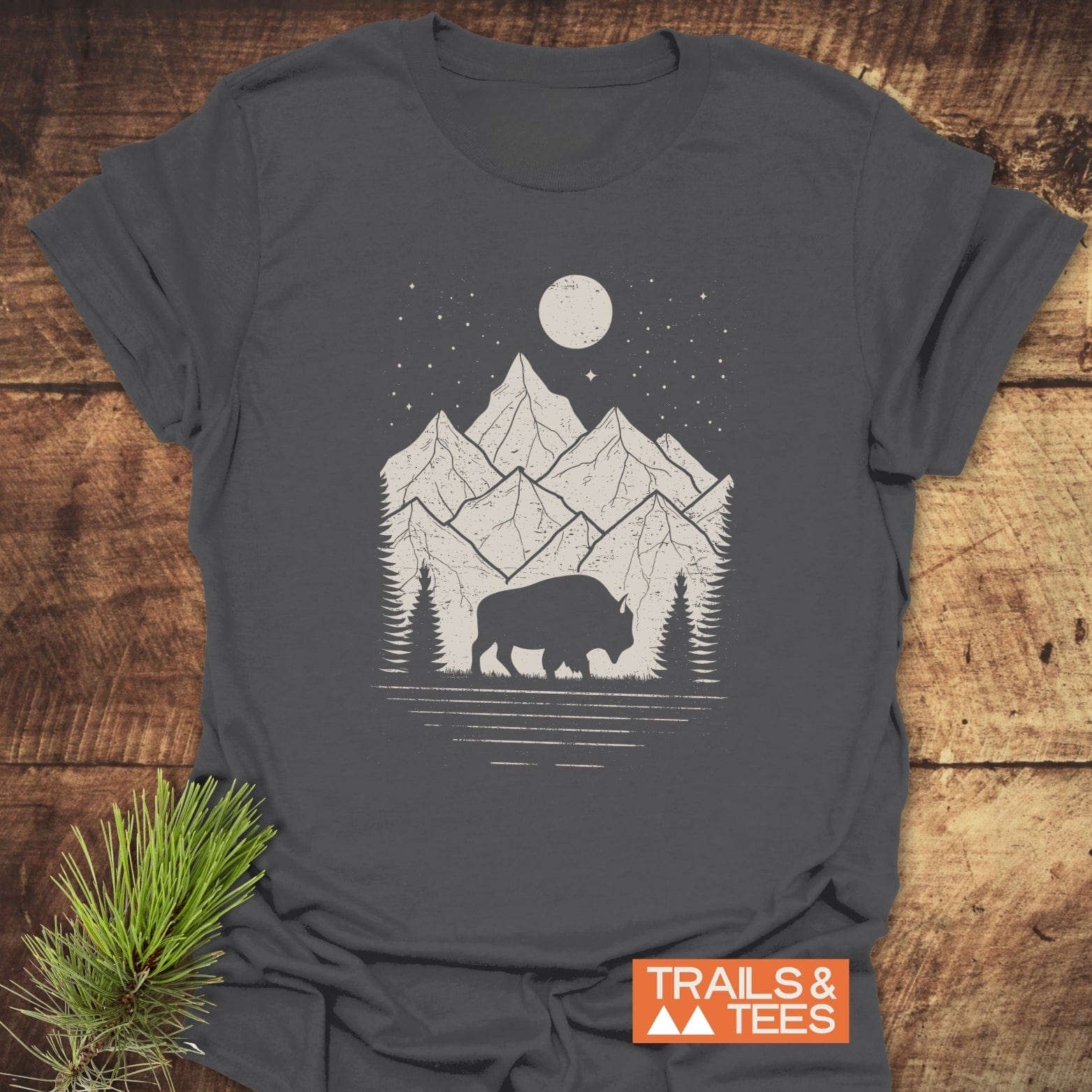 Nightsky Buffalo T-Shirt featuring a grazing bison, pine trees, and mountains under a moonlit sky, crafted from soft cotton for outdoor enthusiasts.