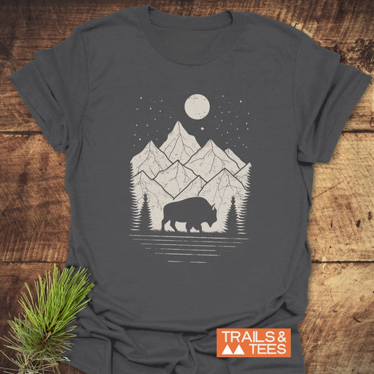 Nightsky Buffalo T-Shirt featuring a grazing bison, pine trees, and mountains under a moonlit sky, crafted from soft cotton for outdoor enthusiasts.