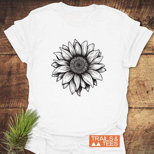 Sunflower T-Shirt featuring a black sunflower line-drawing on a white crew-neck, designed for comfort and durability with an orange TRAILS & TEES logo.