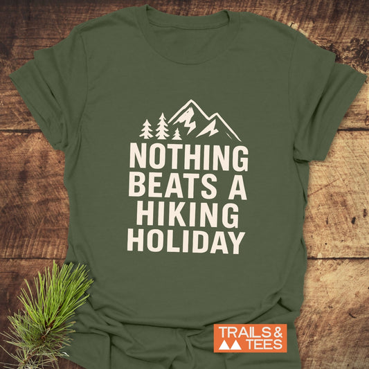 Nothing Beats A Hiking Holiday T-Shirt featuring bold white text and a mountain icon, laid flat with a pine sprig beside it for styling.