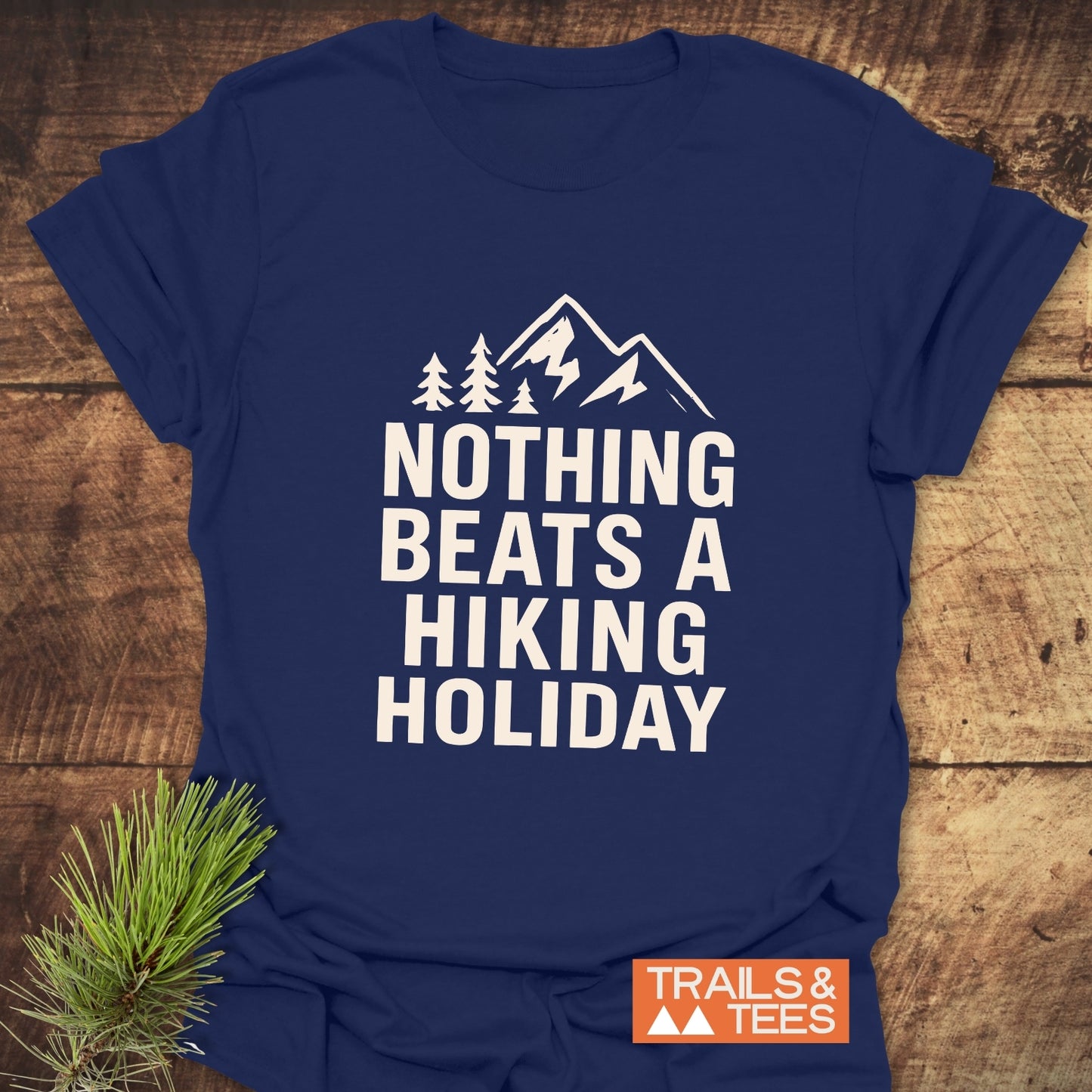 Navy-blue T-shirt with mountain graphic and slogan NOTHING BEATS A HIKING HOLIDAY. Features a small TRAILS & TEES logo. Pine sprig accent.