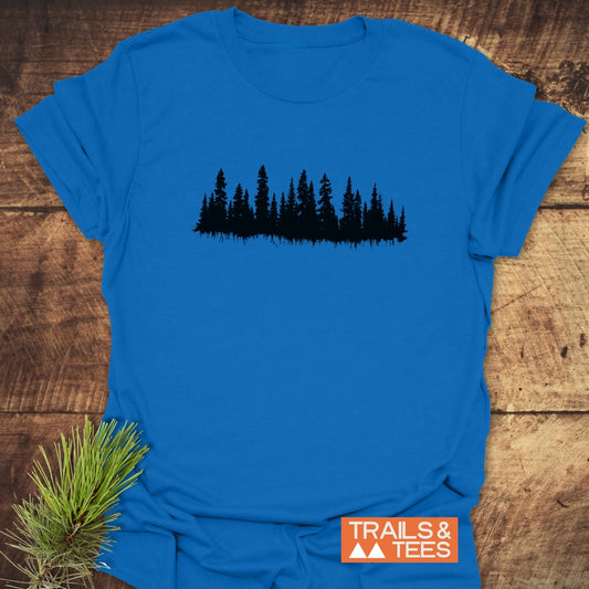 Trees Silhouette T-Shirt with evergreen tree design and Trails & Tees logo, crafted from soft ring-spun cotton for outdoor adventures, laid on wood with pine styling.