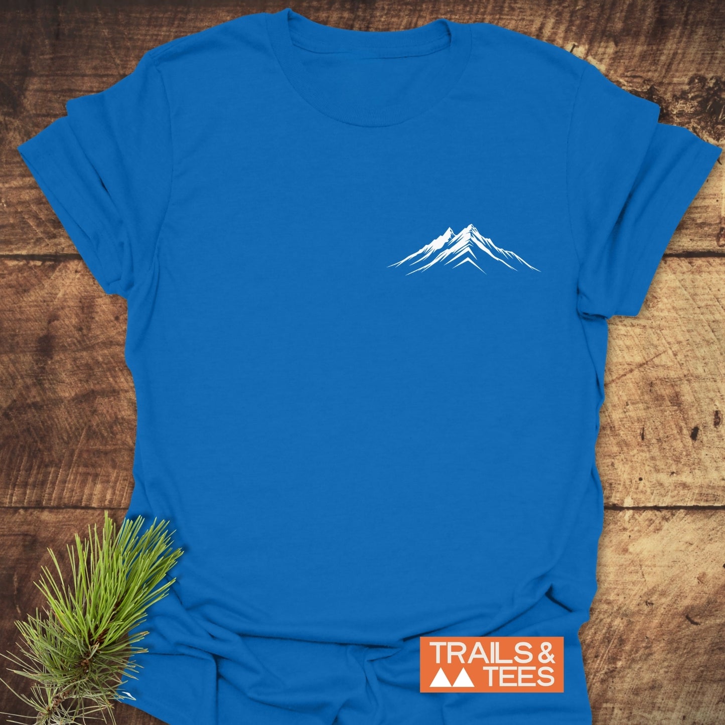 Mountains Logo T-Shirt on wooden surface, featuring a minimalist mountain design on the chest. Made from soft, lightweight cotton for comfort and durability.