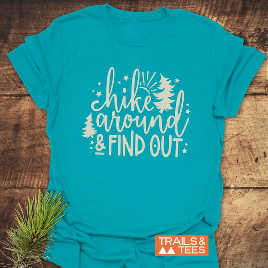 Hike Around And Find Out T-Shirt on wood, featuring white script and block letters with pine-tree and star graphics, conveying a rustic outdoor vibe.