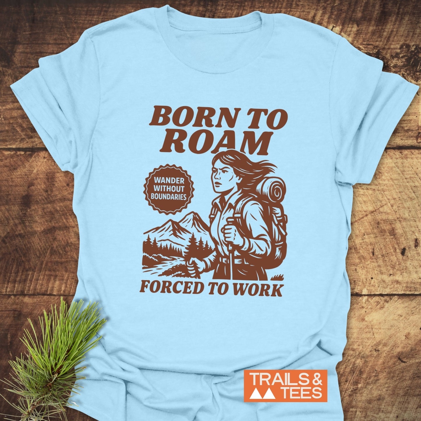 Born To Roam T-Shirt featuring a woman hiker illustration, mountain landscape, and motivational text. Crafted from soft cotton, ideal for outdoor enthusiasts.