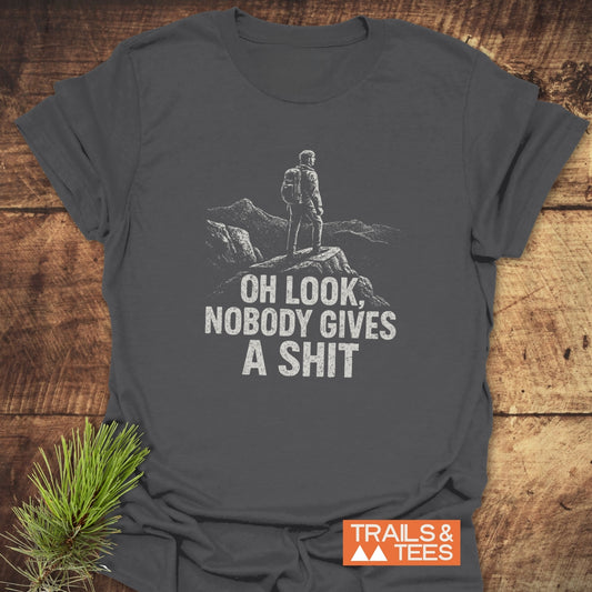 Dark-gray Oh Look! T-Shirt with a hiker graphic, mountain backdrop, and humorous text, featuring durable prints and a Trails & Tees logo.
