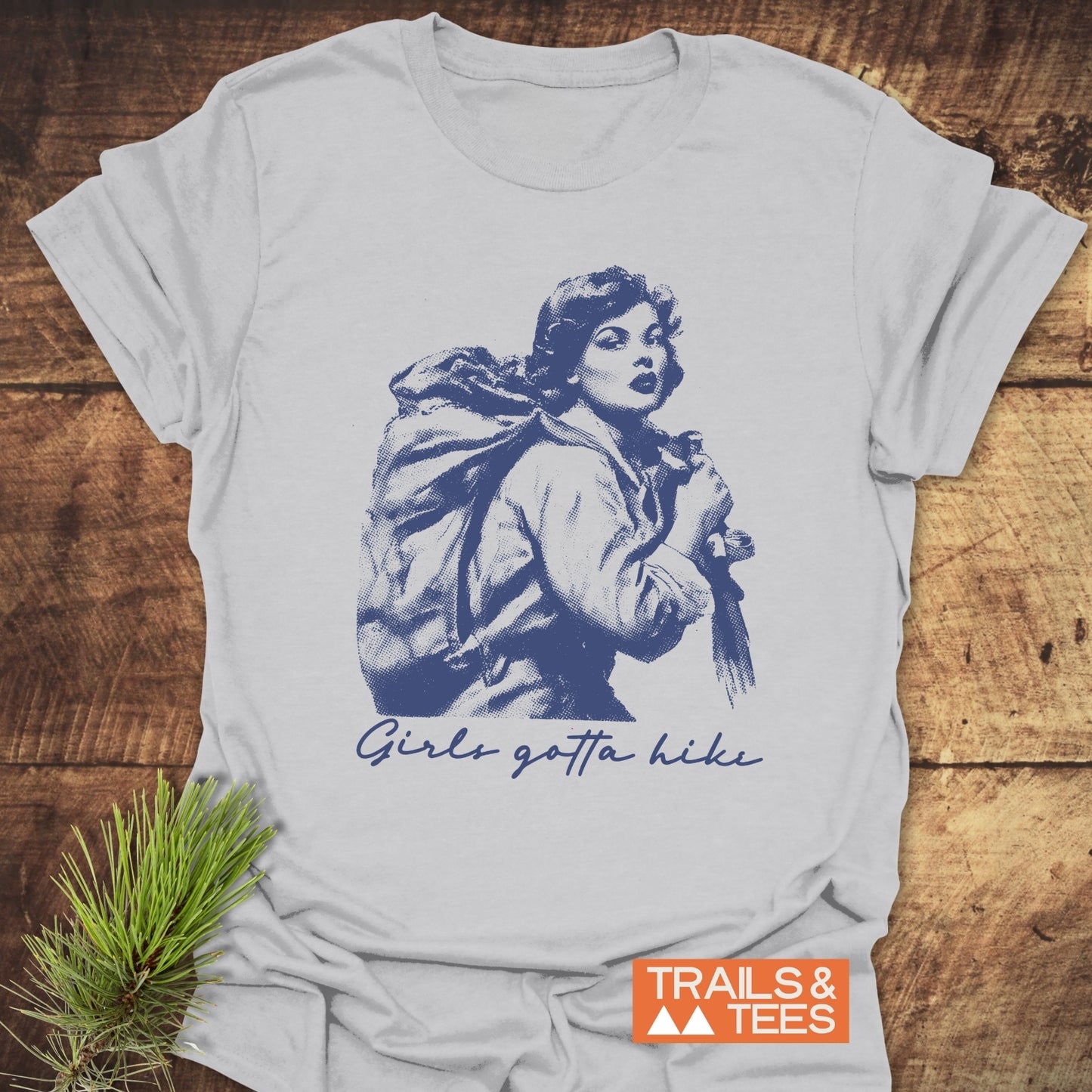Girls Gotta Hike T-Shirt features a blue vintage-style illustration of a woman hiking, with Girls gotta hike slogan, on soft, light-grey cotton.