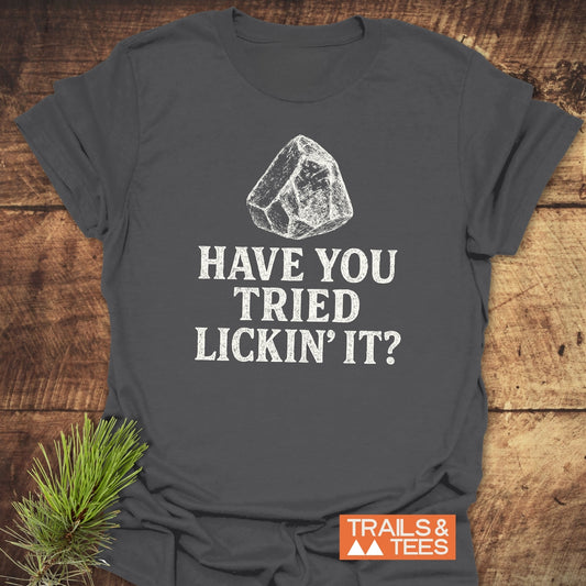 Have You Tried... Rock Lover T-Shirt on wood surface, featuring a sketched rock icon, bold lettering, and TRAILS & TEES logo.