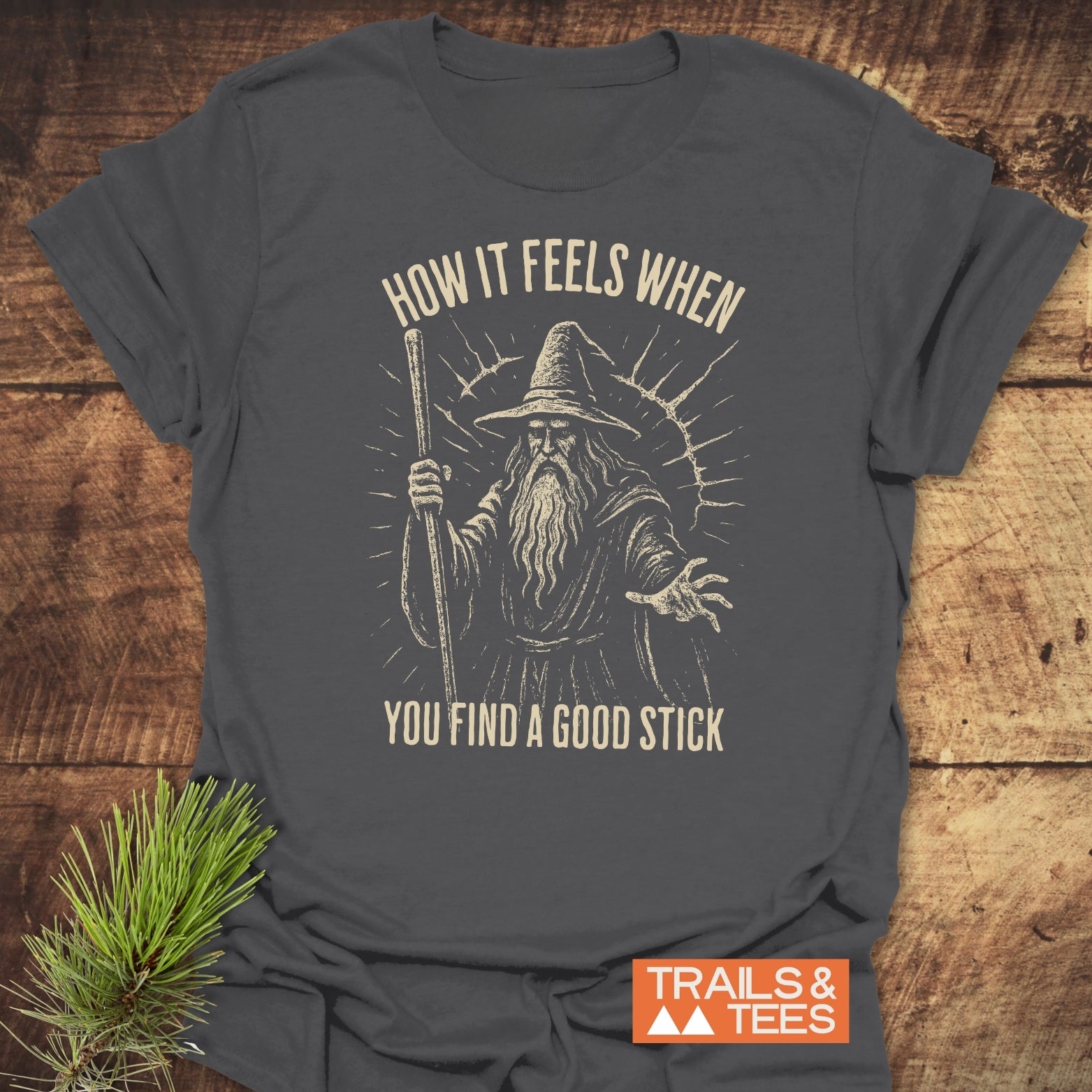 Good Stick T-Shirt: Heather-gray cotton with a vintage wizard illustration, cream caption, and TRAILS & TEES logo. Designed for comfort and durability.