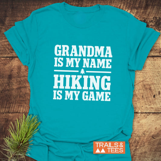 Grandma Hiking T-Shirt, folded with pine sprig, features bold white lettering and icon. Made from soft ring-spun cotton, showcasing durable DTF prints.