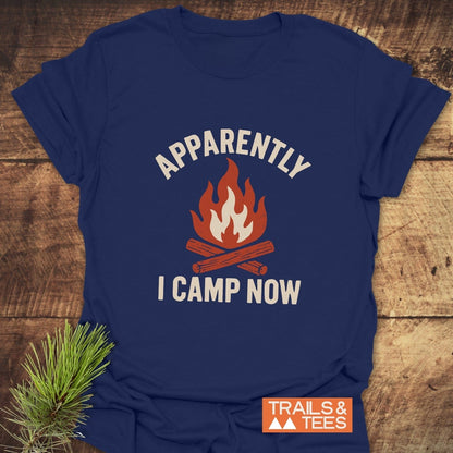 Apparently Camping T-Shirt featuring a campfire print, displayed on wood. Soft, durable ring-spun cotton, pre-shrunk for fit. Trails & Tees logo visible.