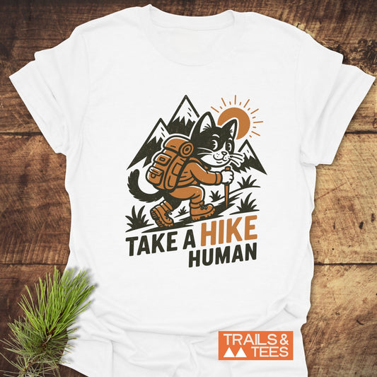 Take A Hike Human T-Shirt featuring a cartoon cat in hiking gear with mountains and sunrise, crafted from soft cotton for outdoor enthusiasts.
