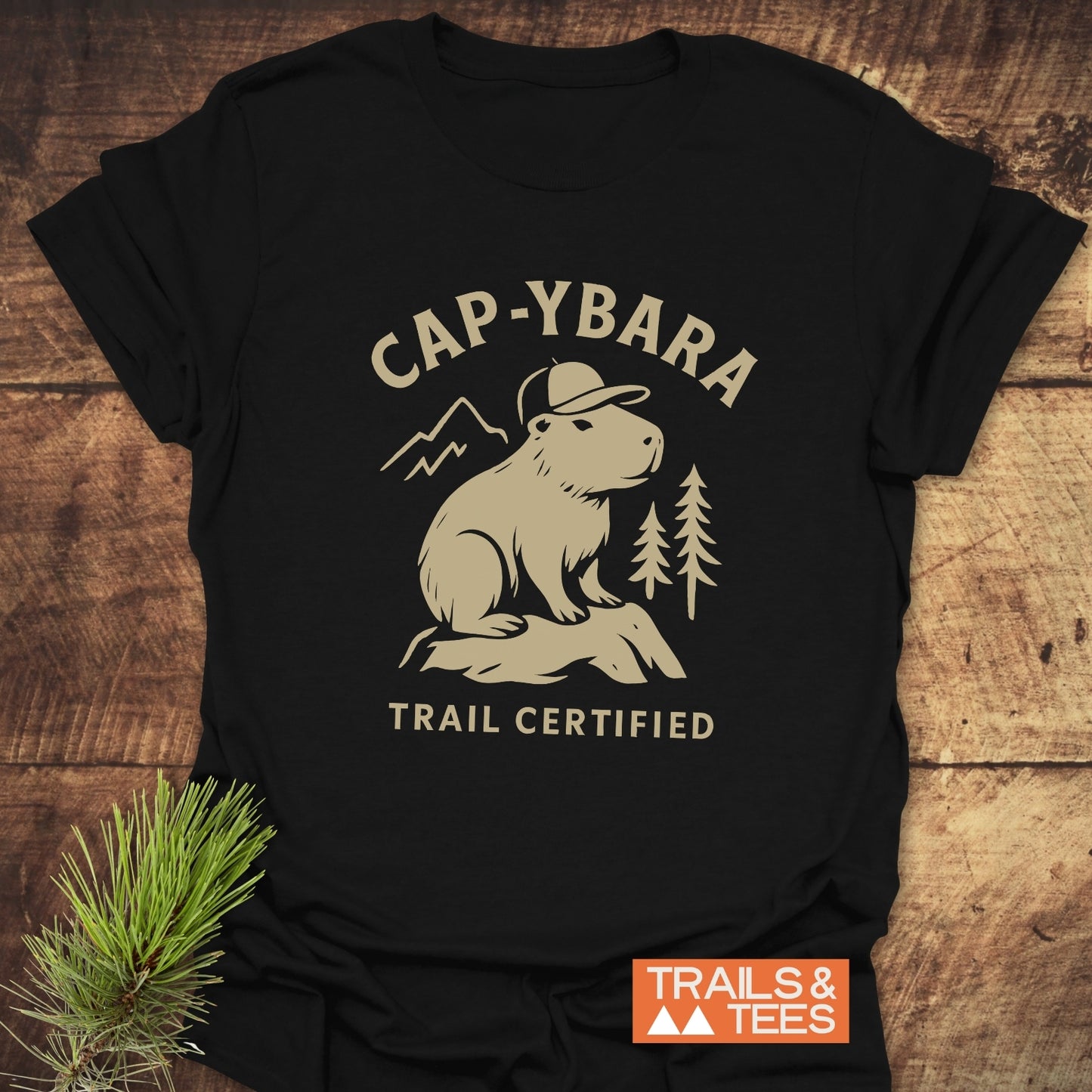 Cap-ybara T-Shirt featuring a capybara graphic with mountain scenery, emphasizing trail-certified comfort and durability. Ideal for outdoor enthusiasts, crafted from soft cotton.