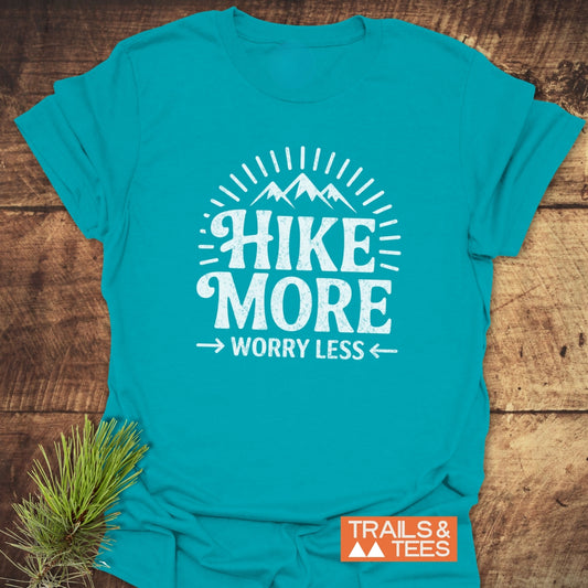 Teal Hike More Worry Less T-Shirt with mountain graphic, laid on wood, featuring durable DTF prints and Trails & Tees logo.