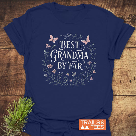 Navy-blue Best Grandma Flower T-Shirt with hand-lettered slogan, floral wreath, and butterflies, on rustic wood. Soft, durable cotton, pre-shrunk, and eco-friendly print.
