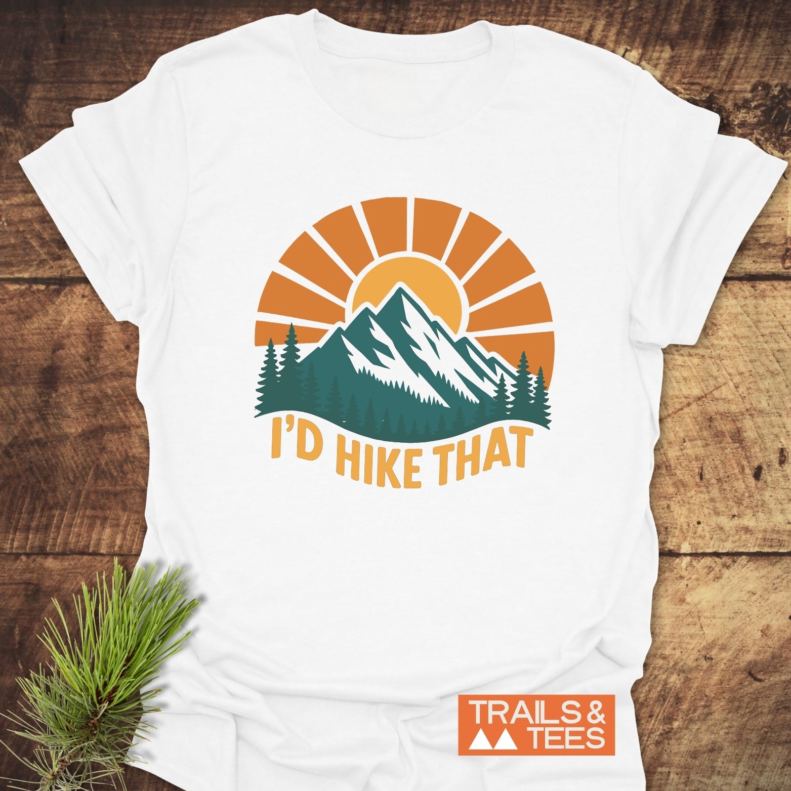 I'd Hike That T-Shirt featuring a green mountain and pine scene with 'TRAILS & TEES' logo, perfect for outdoor enthusiasts and everyday comfort.