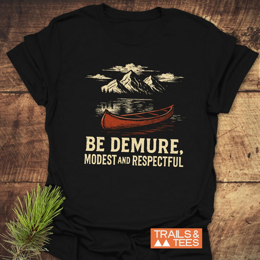 Be Demure Canoe T-Shirt featuring a mountain lake graphic with a red canoe, crafted from soft cotton for comfort and durability, ideal for outdoor enthusiasts.