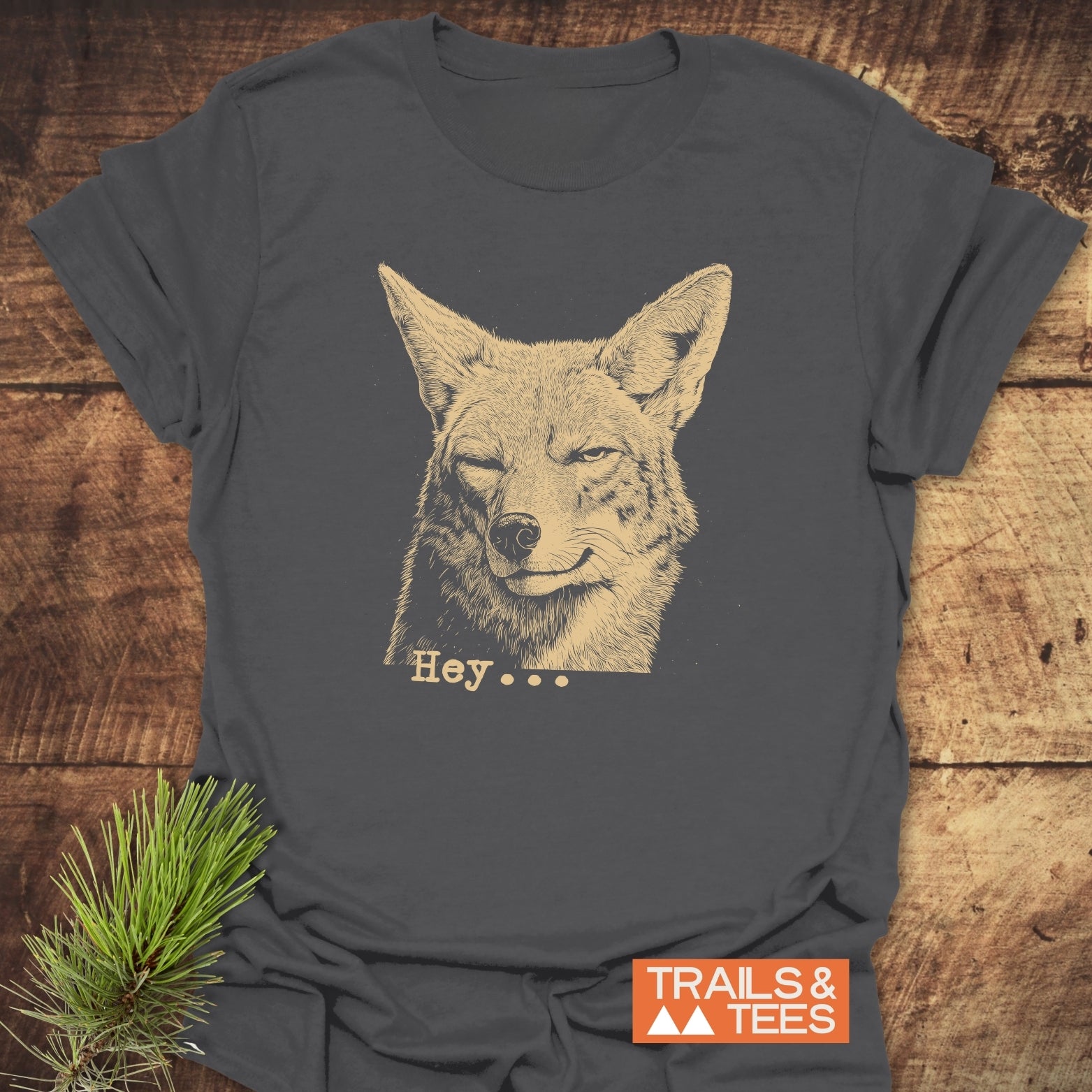 Hey... Coyote Funny T-Shirt featuring a sketch of a fox head winking, laid on wood with a pine sprig, ideal for outdoor enthusiasts.