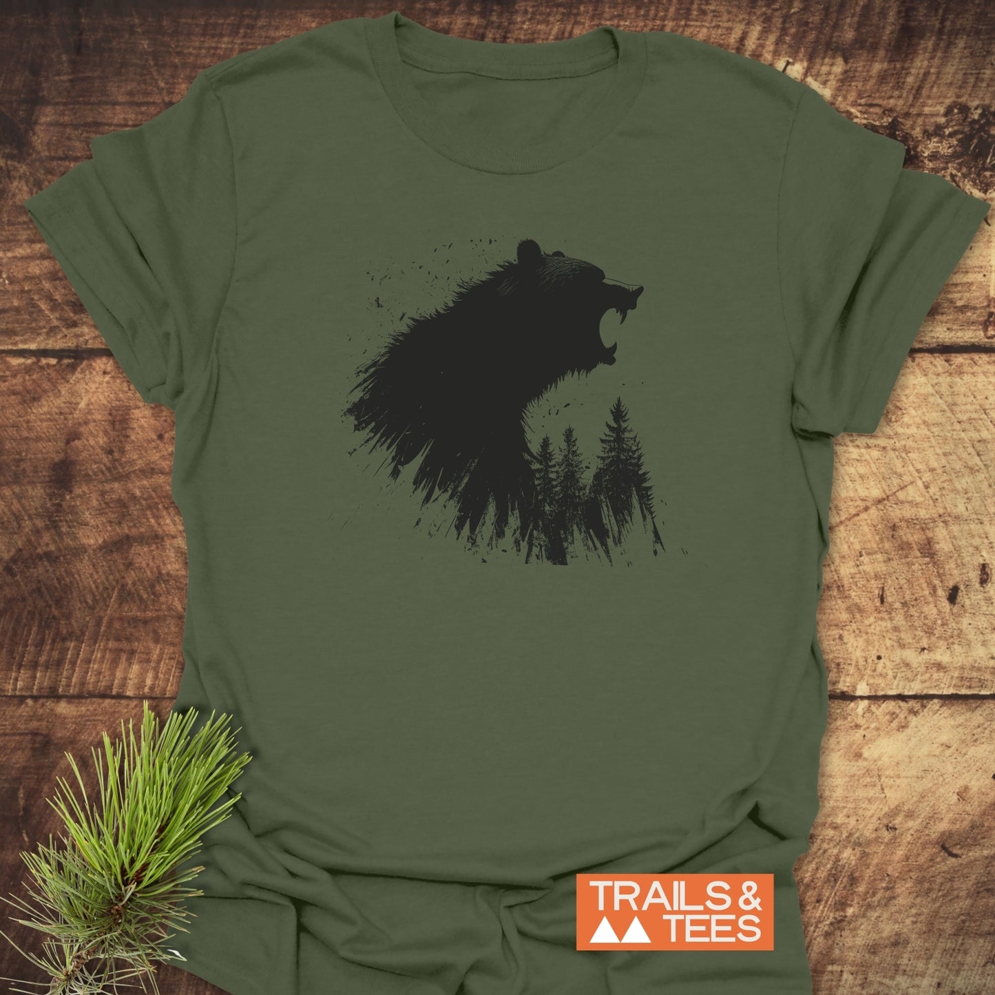 Roaring Bear Forest T-Shirt featuring a black bear graphic on olive-green fabric, laid on wood. Soft ring-spun cotton, durable print, by Trails & Tees.