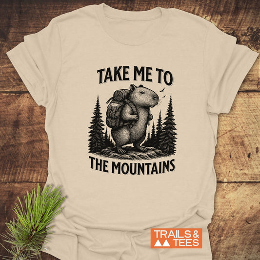 Capybara Mountains T-Shirt with hiking rodent illustration and TAKE ME TO THE MOUNTAINS text, emphasizing outdoor adventure. Features soft cotton and durable prints.